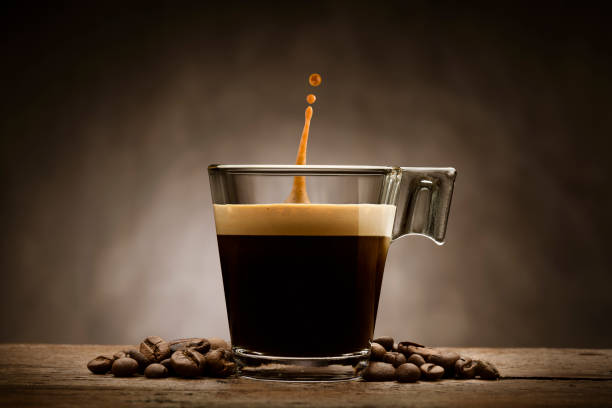 black coffee in glass cup with coffee beans and jumping drop, on wooden table